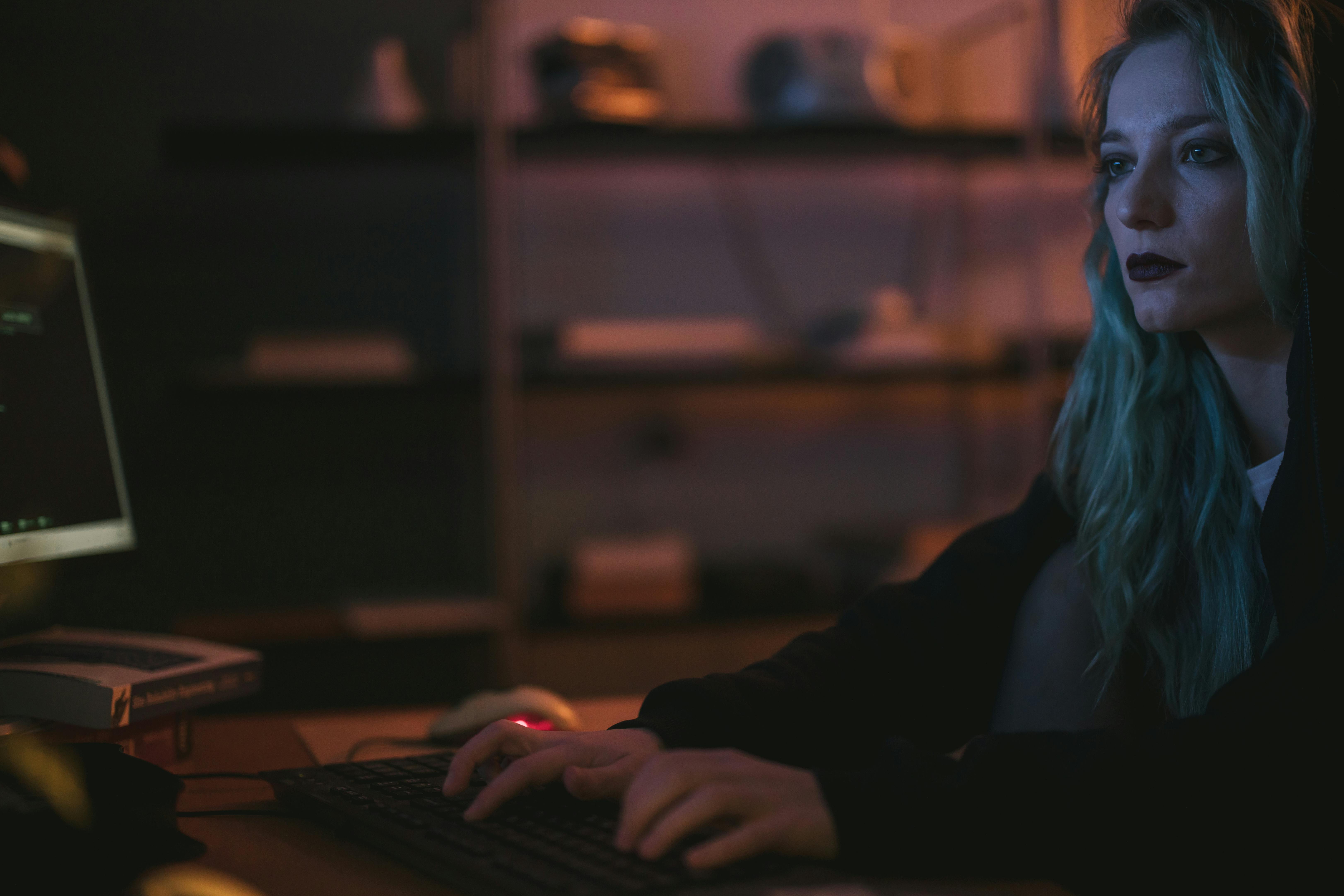 Woman sitting in front of computer typing on keyboard with dark background.
